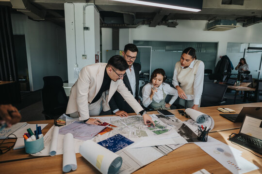 A group of people collaborate intensely on architectural plans in a modern office. The project leader, using crutches, leads the discussion while colleagues examine paperwork and blueprints. - Powered by Adobe