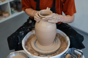 Close-up of a potter's hands making a ceramic vase on a potter's wheel. 