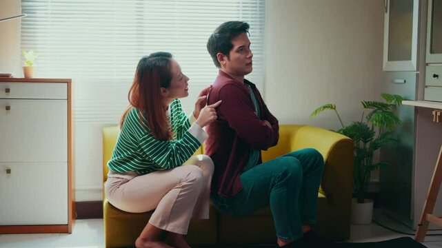 Frustrated asian woman standing on living room sofa, arguing with partner deliberately avoiding eye contact during heated relationship tension