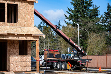 Heavy duty work truck with conveyer belt boom arm delivering roofing materials to a residential house roof in new housing development, winter construction project job site  © knelson20