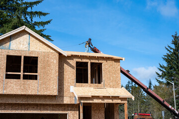 Workman in safety harness on wood framed house roof waiting for roofing materials being delivered...