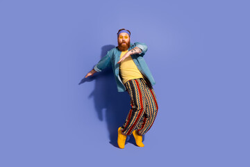 Stylish bearded man dancing in vibrant casual outfit on purple background, showcasing fashion and joyful lifestyle