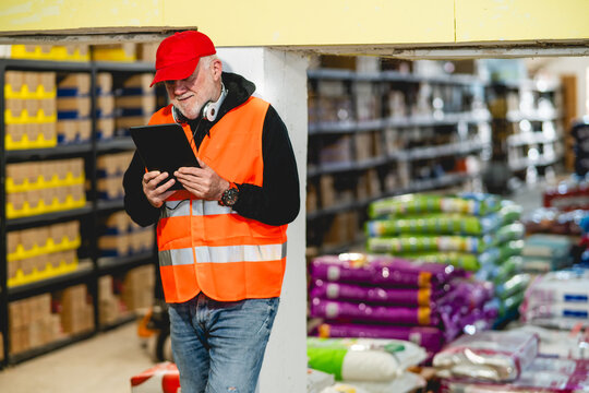 An older worker in a pet food warehouse prepares deliveries of goods for pet stores.