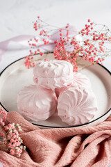Pink berry marshmallow zephyr on white plate on a light background next to pink ribbons and flowers. White and pink zefyr made from applesauce and egg white. Low-calorie sweets. Vegan marshmallow.	
