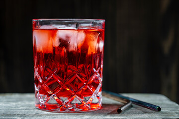 Red cocktail in crystal glass on wooden background, closeup. Summer ice drink - tea or juice with ice cubes on wooden table, copy space