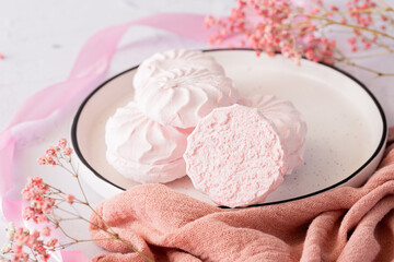 Pink berry marshmallow zephyr on white plate on a light background next to pink ribbons and flowers. White and pink zefyr made from applesauce and egg white. Low-calorie sweets. Vegan marshmallow.