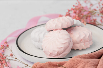 White and pink marshmallow zephyr on white plate on a light background next to pink ribbons and flowers. White zefyr made from applesauce and egg white. Low-calorie sweets. Vegan marshmallow.	