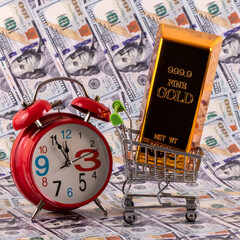 999 fineness gold bar in miniature shopping cart with $100 bills in background