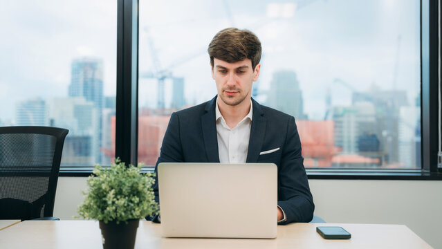A man in a suit is sitting at a desk with a laptop