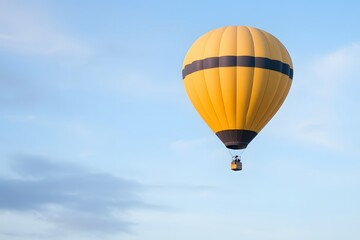 Vibrant yellow hot air balloon soaring against a clear blue sky with soft clouds in the background