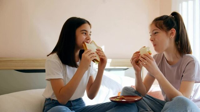 Two happy girls enjoying sandwiches together in a cozy bedroom