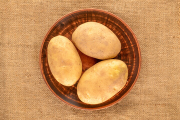 Unpeeled raw potatoes with kitchen utensils on jute cloth, top view, close-up.