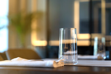 A transparent glass stands on a table against the backdrop of a restaurant. Cloth napkins. Elegant style