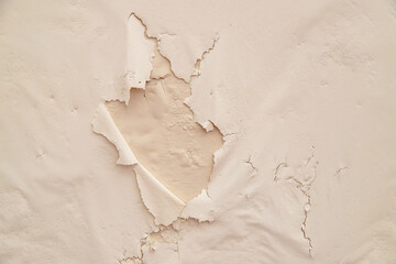 A close-up of a cracked and peeling wall reveals layers of old paint and plaster, showcasing the effects of time, weather, and neglect in an aged interior or abandoned space.