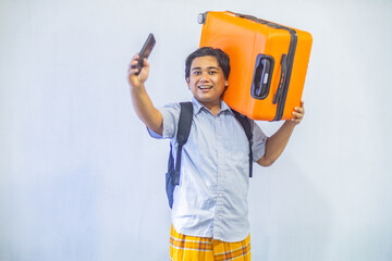 Portrait Asian muslim man carrying suitcase while holding mobile phone with copy space inside. Concept Going home for Eid Mubarak. Isolated image on white background