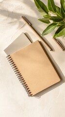 Beige notebook, pens, and plant on a light surface