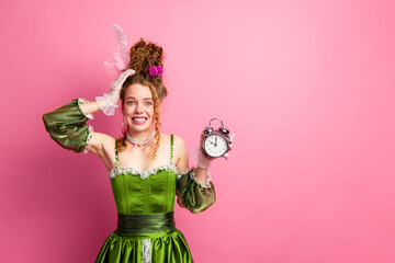 Elegant young woman in vintage green attire holding a clock with expression of concern against a pink background