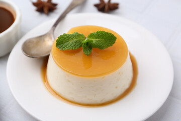 Tasty pudding with caramel sauce served on white tiled table, closeup