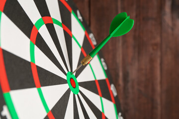 Dart board with arrow on wooden background, closeup. Space for text