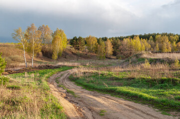 Beautiful country landscape in spring, dirt road, sunset, dramatic sky