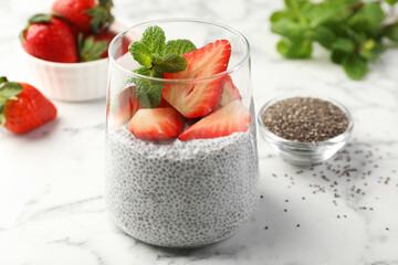 Delicious chia pudding with strawberries and mint in glass on white marble table, closeup