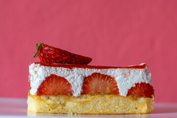 Slice of delicious cream cake with fresh sliced strawberries and red gelatin on pink background