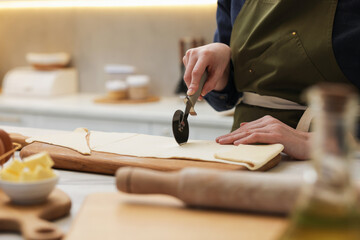 Woman cutting dough at light marble table indoors, closeup. Making croissants