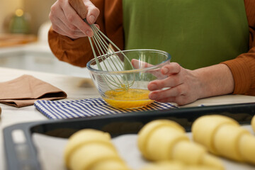 Woman whisking egg wash near raw croissants at white table indoors, selective focus