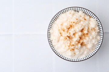 Tasty rice pudding with cinnamon on white tiled table, top view. Space for text