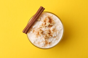 Tasty rice pudding with cinnamon and nuts in glass bowl on yellow background, top view