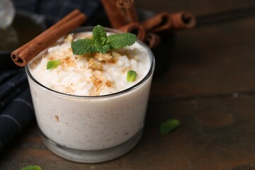 Tasty rice pudding with cinnamon, mint and nuts on wooden table, closeup. Space for text