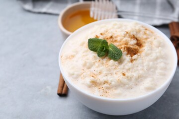 Tasty rice pudding with cinnamon, mint and honey on light grey table, closeup. Space for text