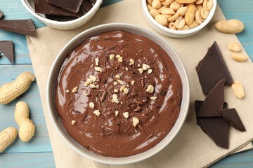 Tasty chocolate pudding in bowl and ingredients on light blue wooden table, flat lay