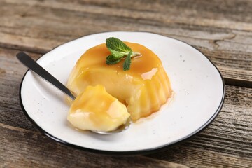 Delicious pudding with caramel sauce and mint served on wooden table, closeup