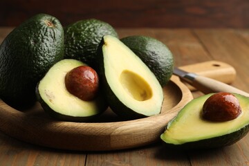 Whole and cut avocados on wooden table, closeup