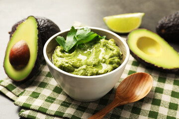 Tasty avocado dip in bowl, parsley and fruits on table, closeup
