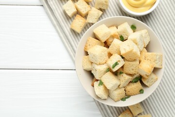 Delicious crispy croutons with parsley and sauce on white wooden table, flat lay. Space for text