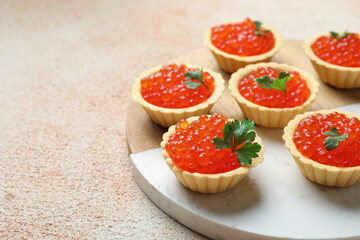 Tartlets with red caviar and parsley on beige table, closeup. Space for text