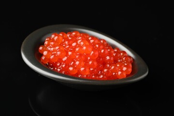 Red caviar on black mirror surface, closeup