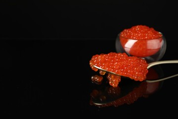 Red caviar on black mirror surface, closeup. Space for text