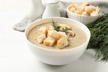 Delicious mushroom cream soup with croutons and dill served on white table, closeup