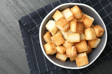 Tasty crispy croutons in bowl on dark textured table, top view. Space for text