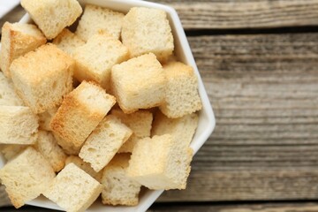 Tasty crispy croutons in bowl on wooden table, top view. Space for text