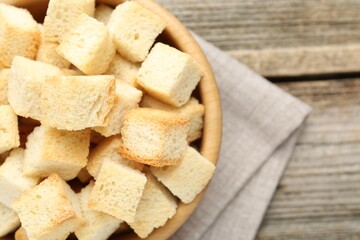 Tasty crispy croutons in bowl on wooden table, top view. Space for text