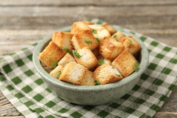 Tasty crispy croutons with cut parsley in bowl on wooden table, closeup