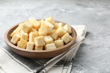 Tasty crispy croutons in bowl on grey textured table, closeup
