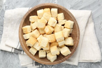 Tasty crispy croutons in bowl on grey textured table, top view