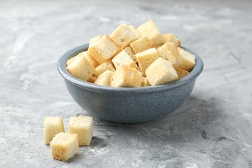Tasty crispy croutons in bowl on grey textured table, closeup