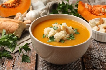 Tasty pumpkin cream soup with croutons and parsley in bowl on wooden table, closeup