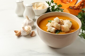 Tasty pumpkin cream soup with croutons and parsley in bowl on white table, closeup